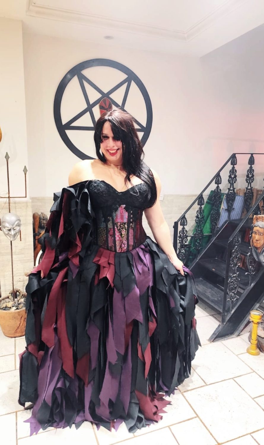 Dirigente do Templo da Serpente Negra em vestido ritual preto e bordô com pentagrama e objetos sagrados ao fundo